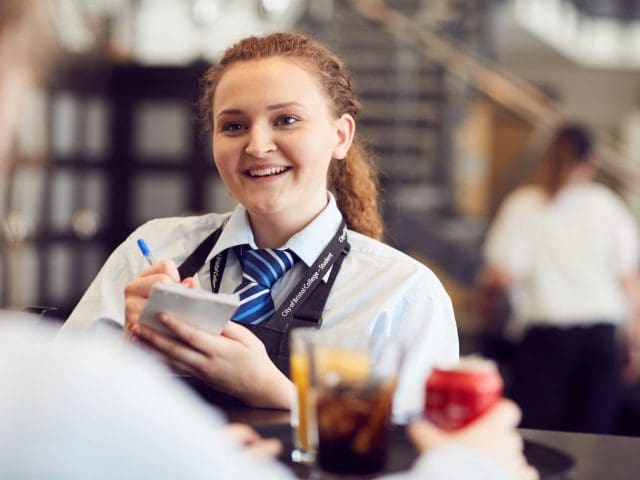 A young, smiling woman from City of Bristol College takes an order
