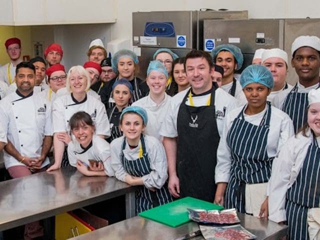 Chefs stand with students in a kitchen