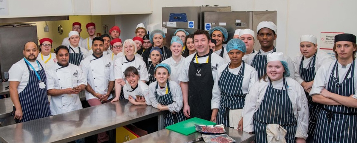 Chefs stand with students in a kitchen