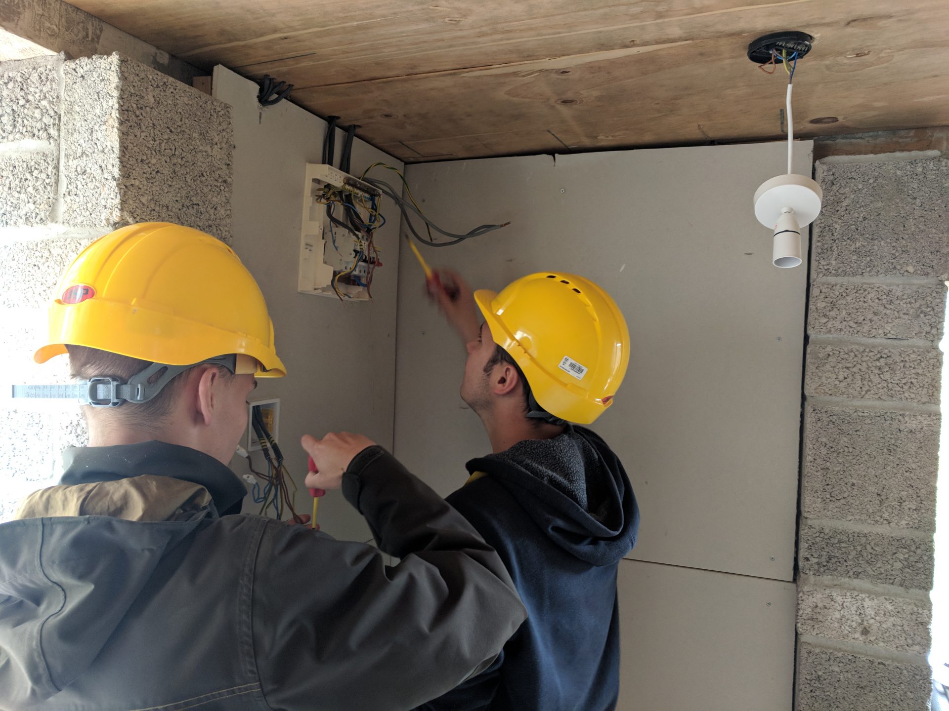 Electrical students in hard-hats work on a fuse box