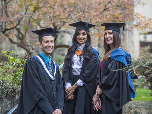 Graduates of a university course and staff stand in gowns