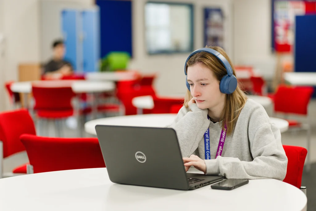 Female student with headphones looks at a laptop.