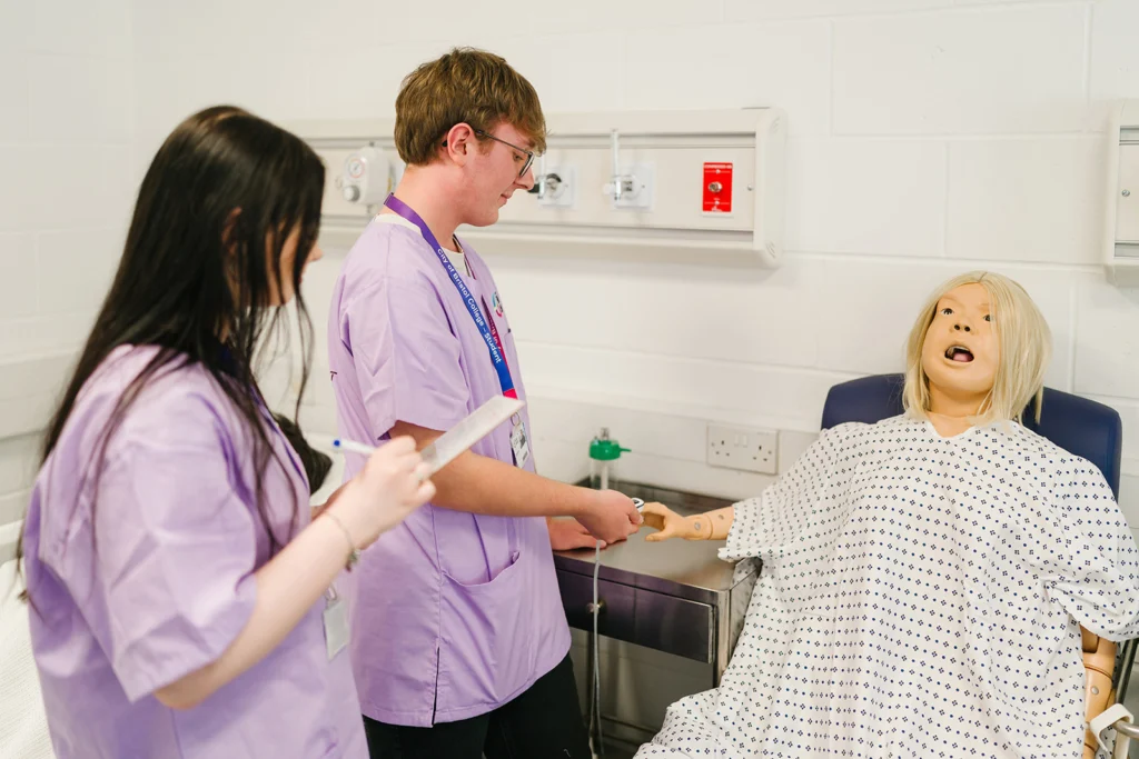 two students performing a check up action on a dummy patient in a clinic setting