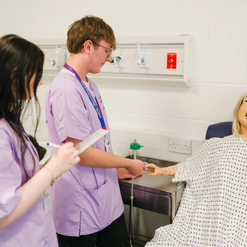two students performing a check up action on a dummy patient in a clinic setting