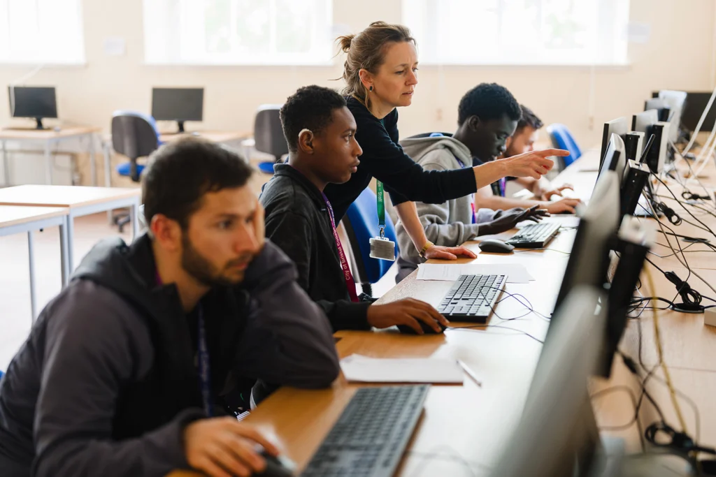 teacher pointing at a screen helping a student sat in a computer class environment
