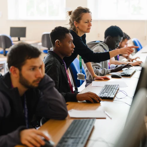teacher pointing at a screen helping a student sat in a computer class environment