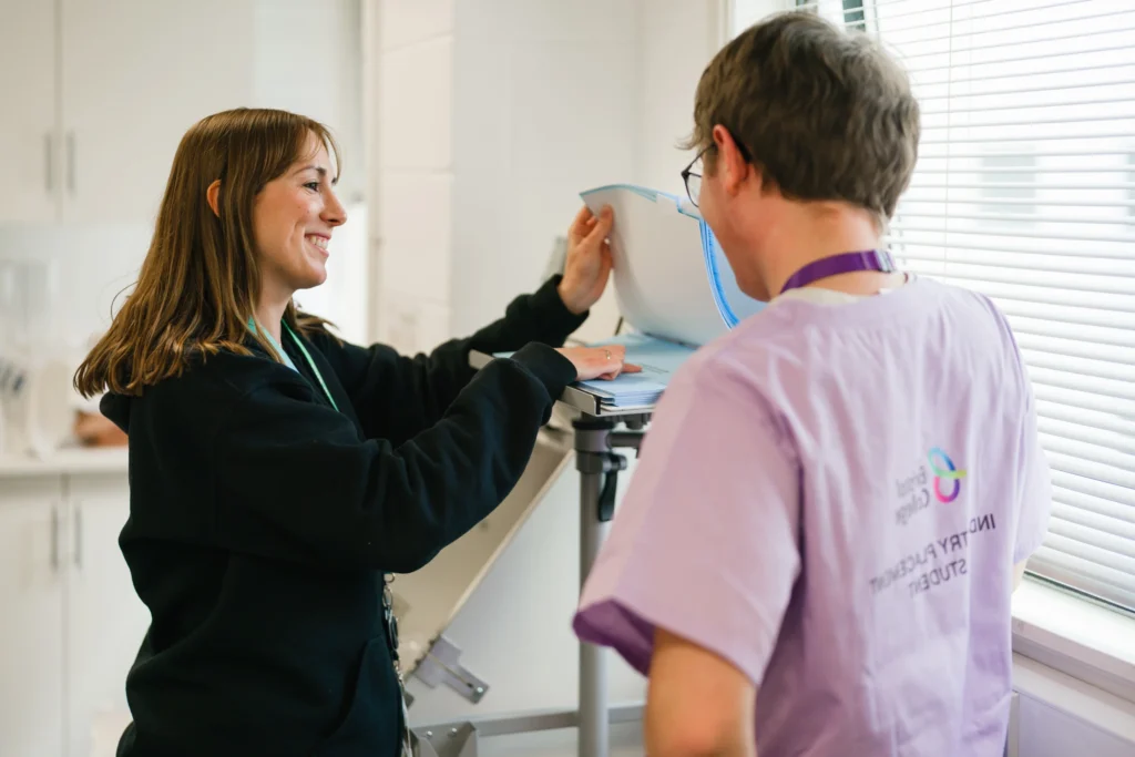 Student wearing scrubs, talking to a Tutor who is flicking through notes.
