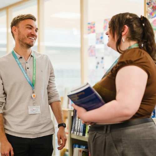 Two adults smiling and having a conversation in a workplace.