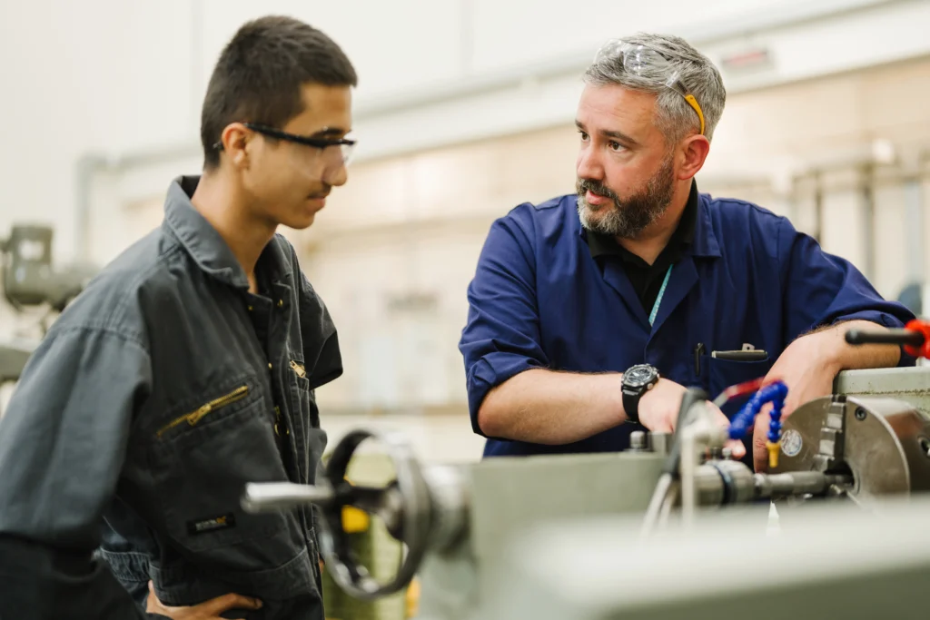 Tutor discussing machinery with a student during a workshop.