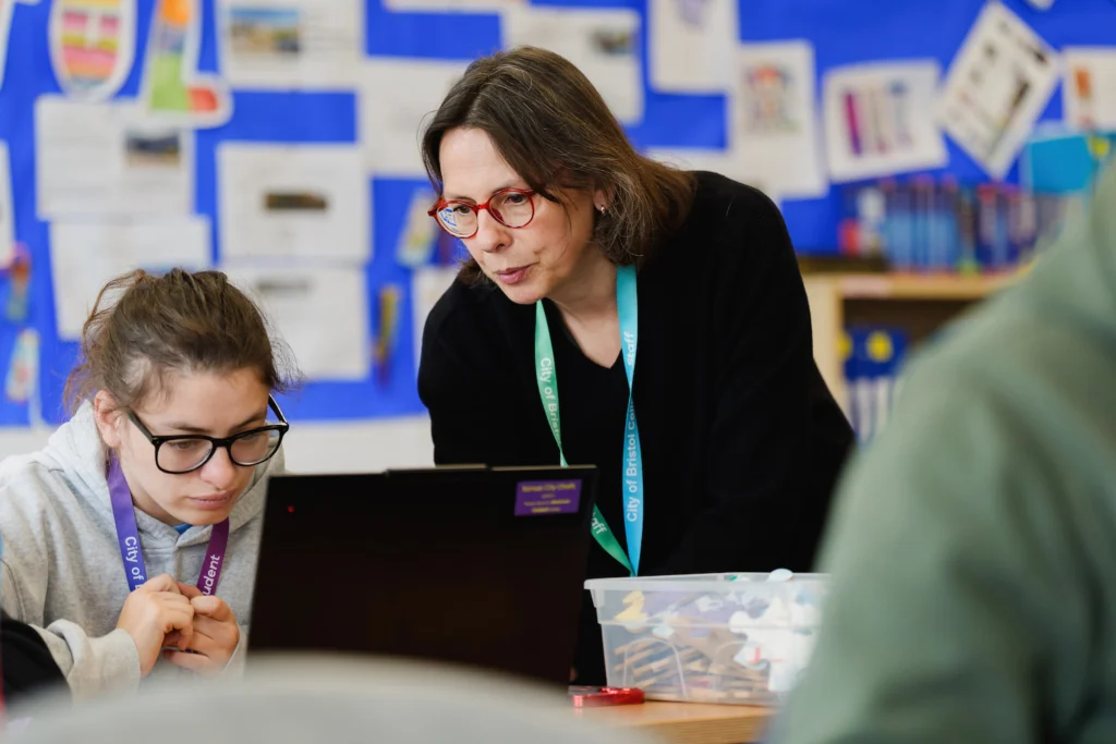 A teacher helping a special education needs student with a task on their laptop in a classroom