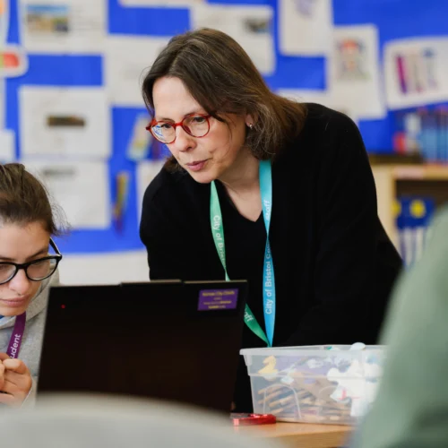 A teacher helping a special education needs student with a task on their laptop in a classroom