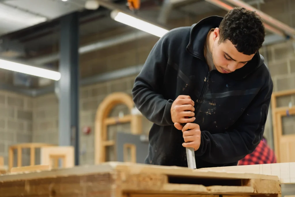 A student holding a chisel doing some work in a workshop setting