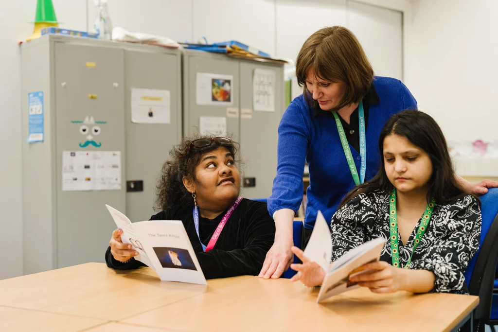 Teacher talks to two student's both reading booklets